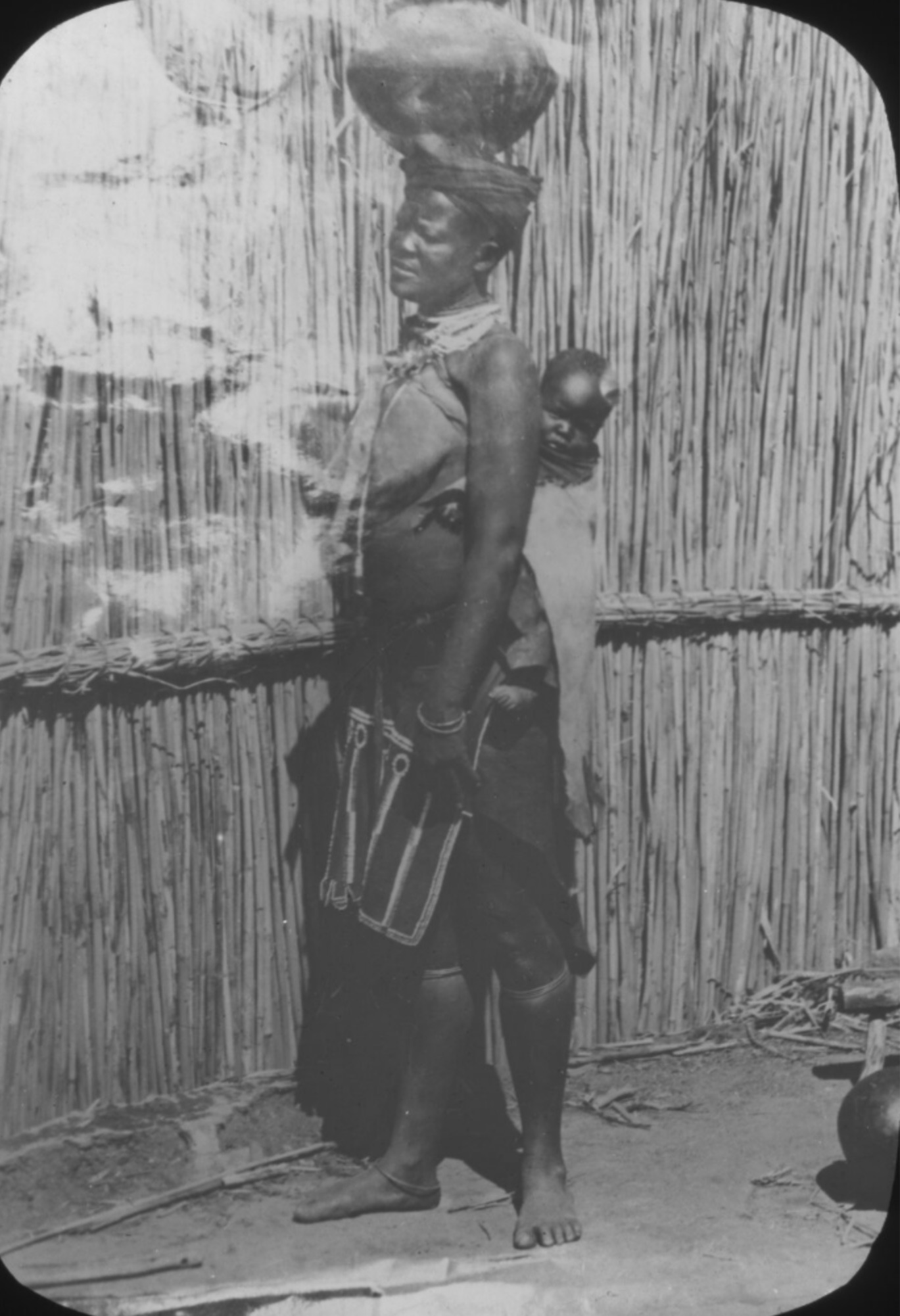 Frau mit einer Art Topf auf dem Kopf und Kind auf dem Rücken.